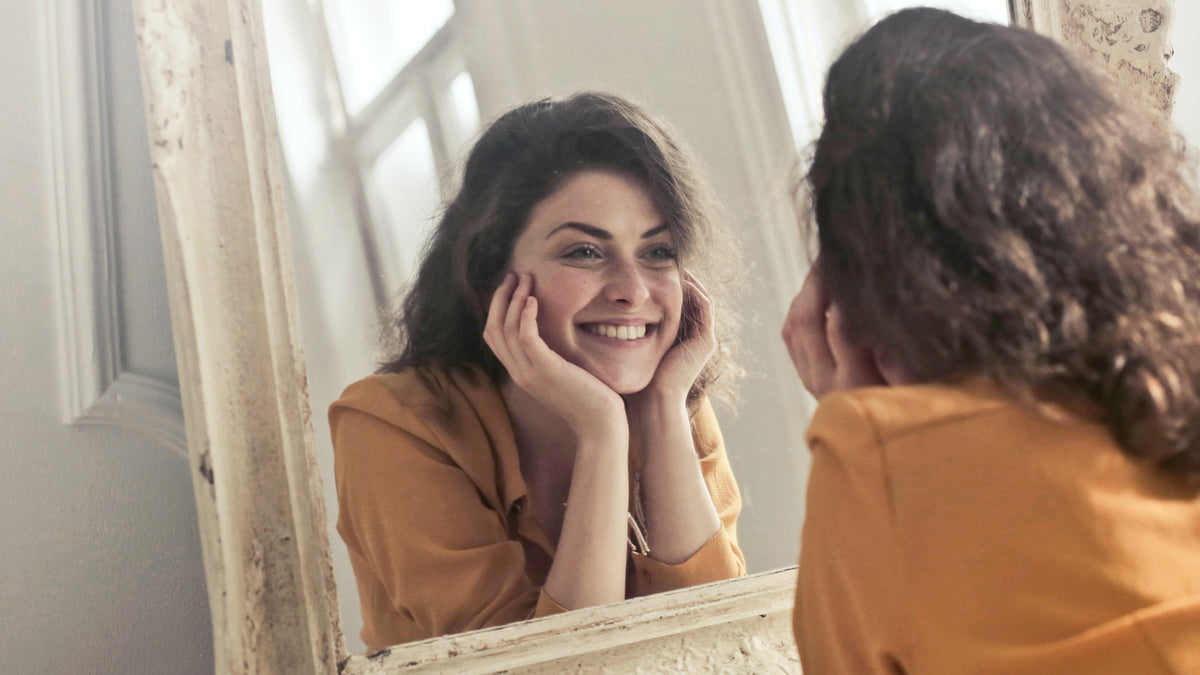 woman-looking-in-mirror-smiling-andrea-piacquadio