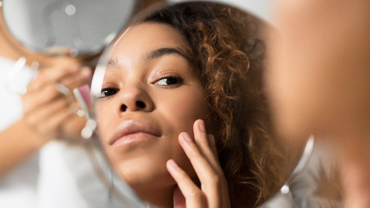 Gorgeous black woman looking at her skin in the mirror