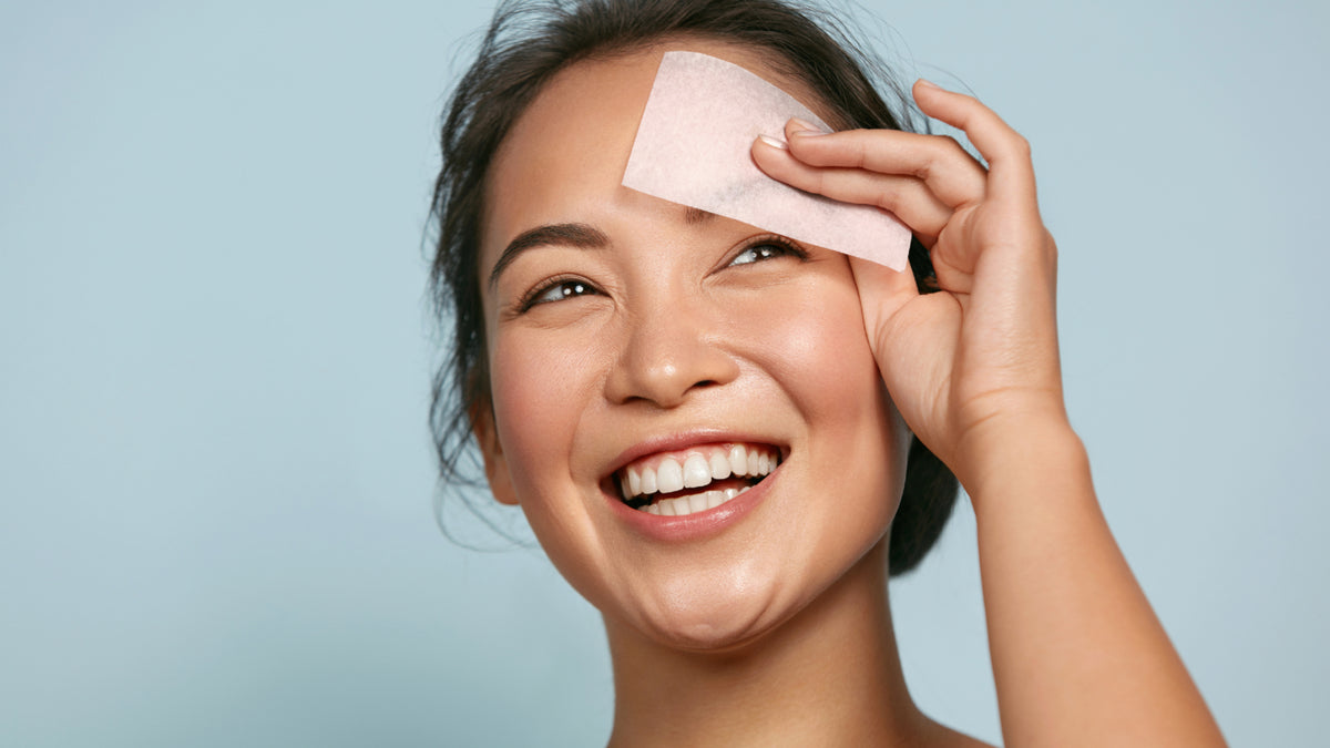 Girl with beautiful skin blotting face with oil control paper