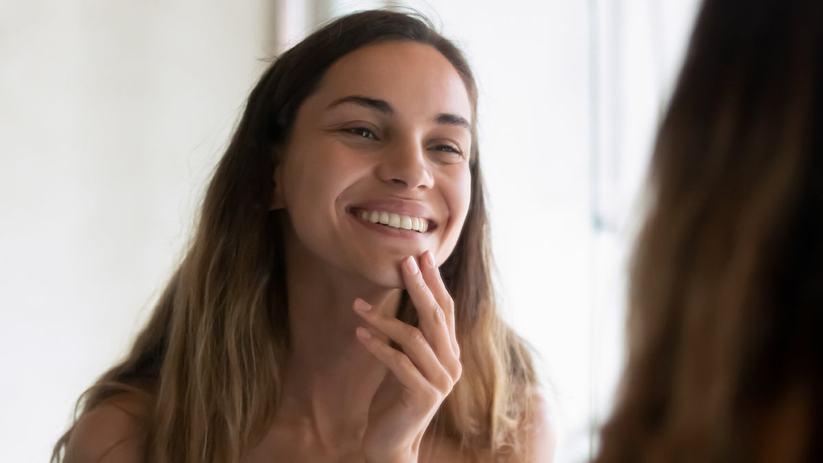 dark blonde girl smiling and checking skin in the mirror