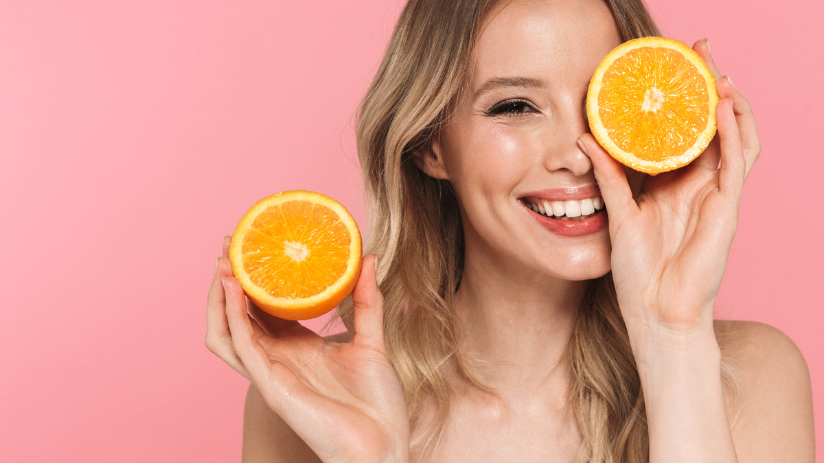 happy blonde girl on pink background holding two halves of an orange