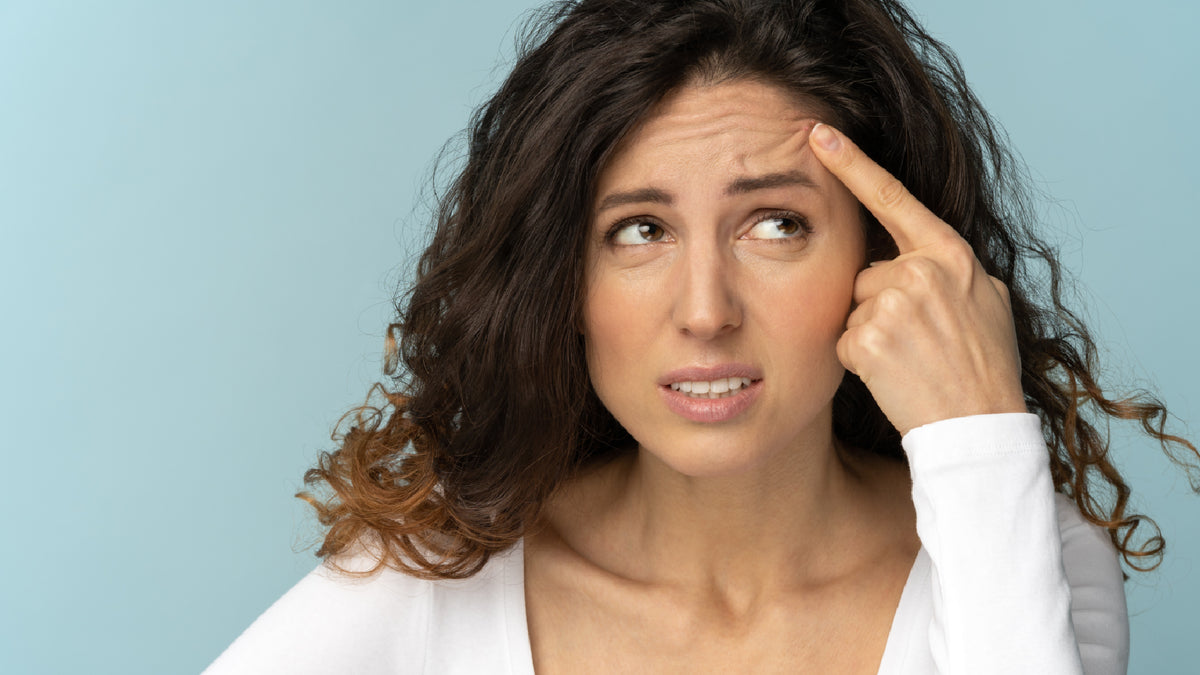 brunette woman grimacing and pointing to acne pimple