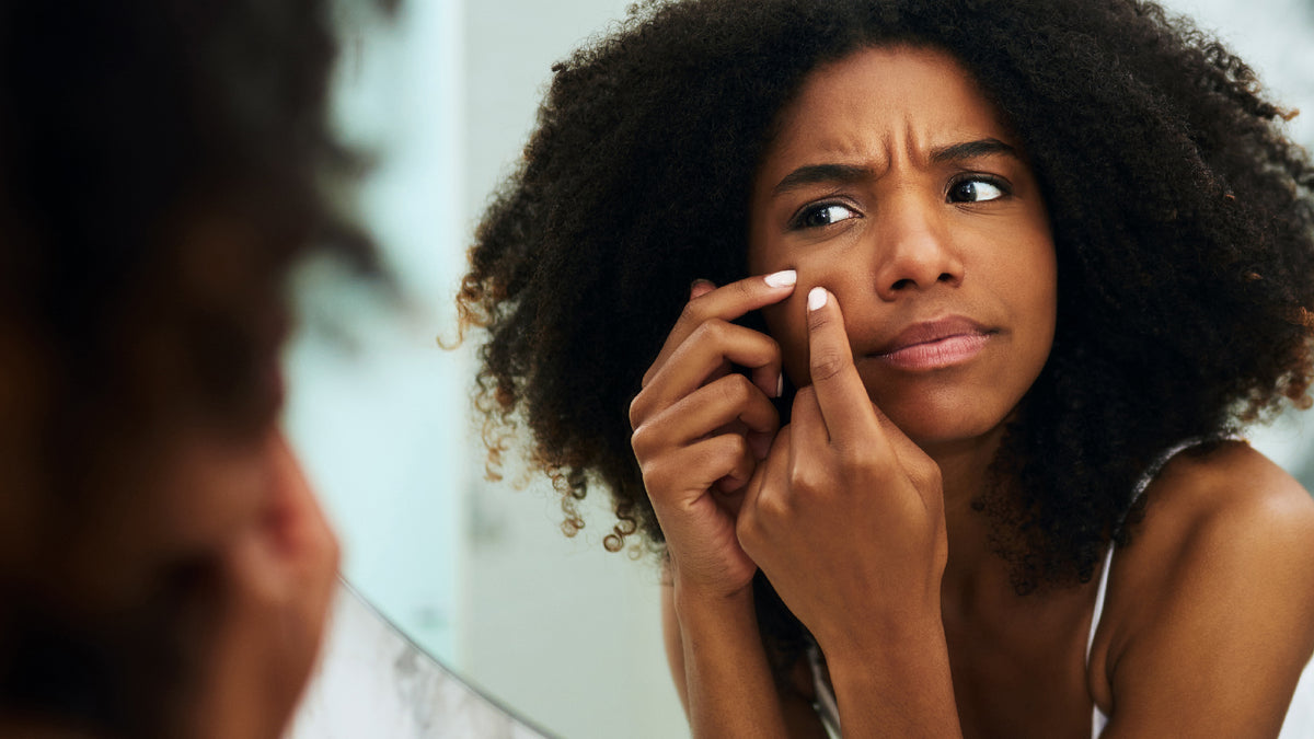 black woman squeezing pimple in the mirror