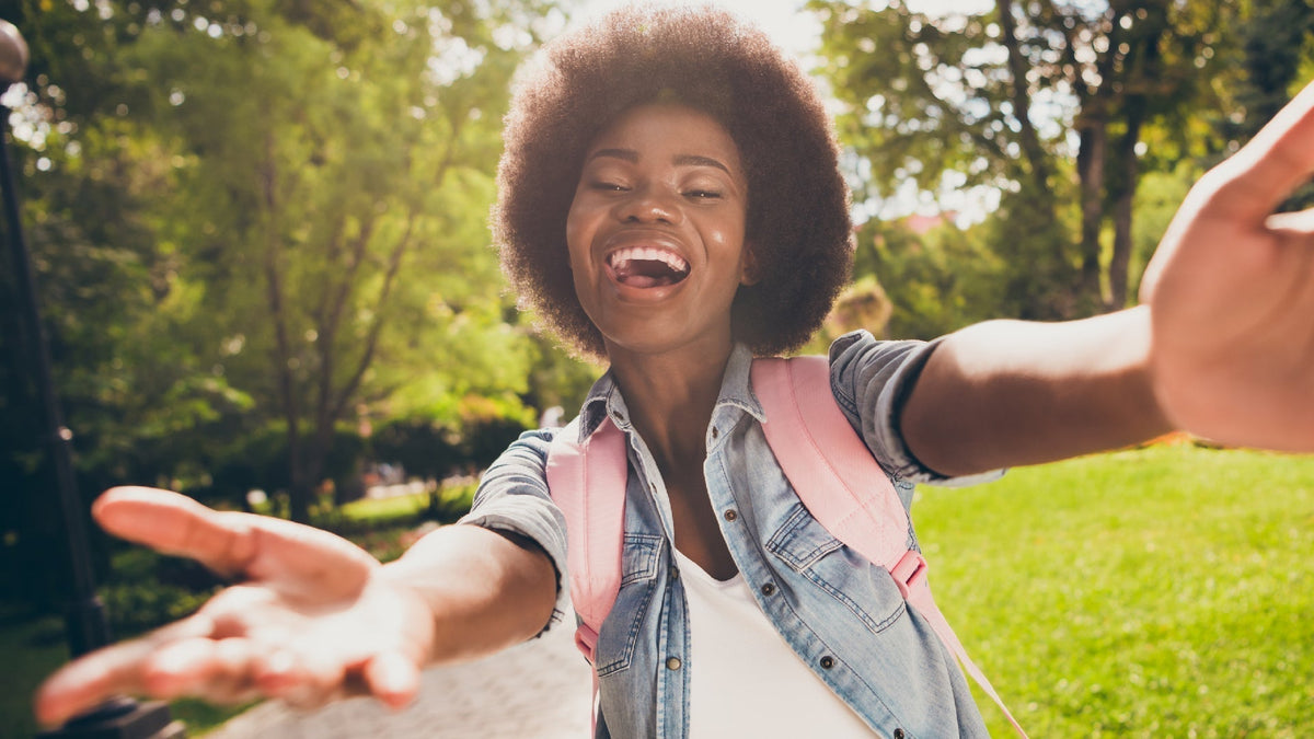 young black woman laughing outside with open arms