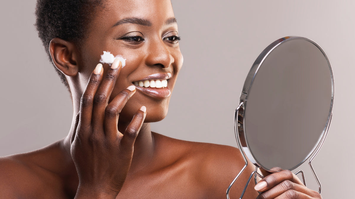 Black girl with beautiful skin looking in mirror and applying face cream