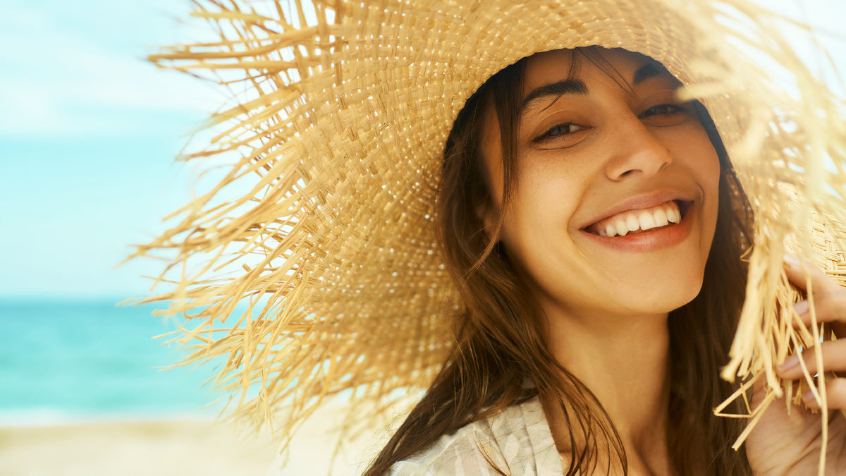 brunette girl in straw hat on beach smiling