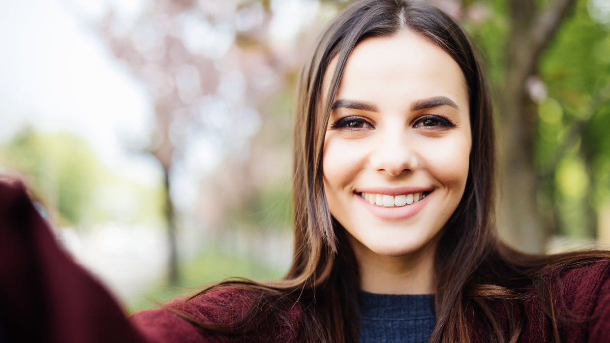 young brunette woman outside smiling taking selfi