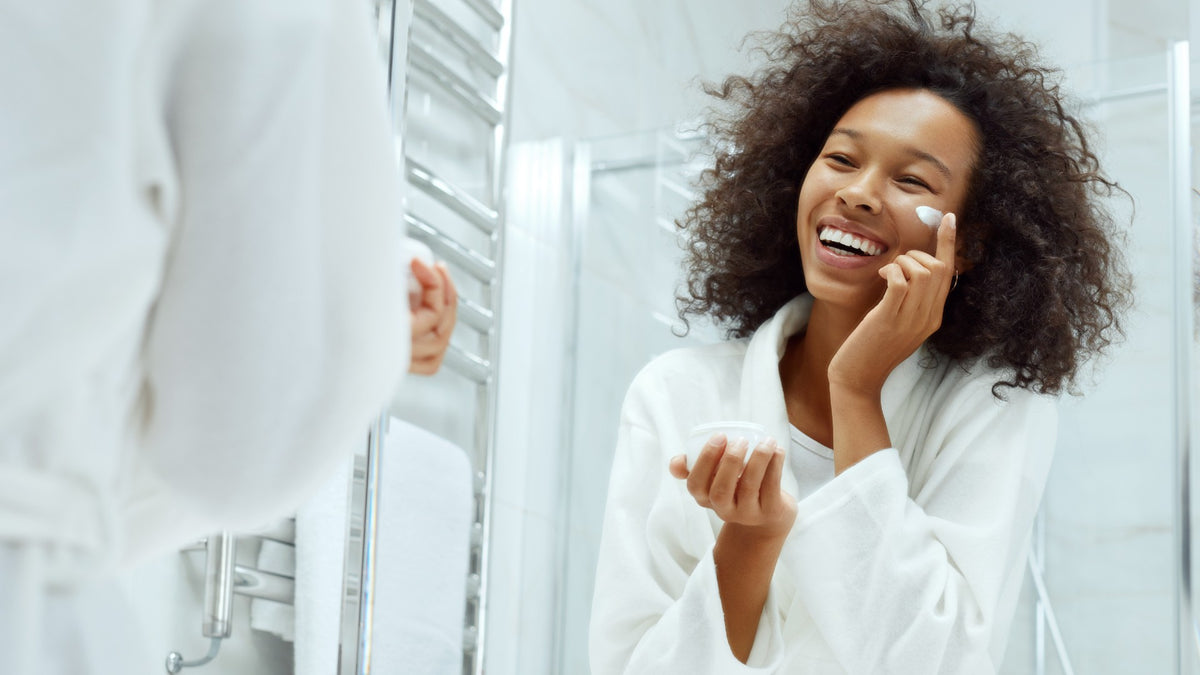 black woman applying skin product in the mirror