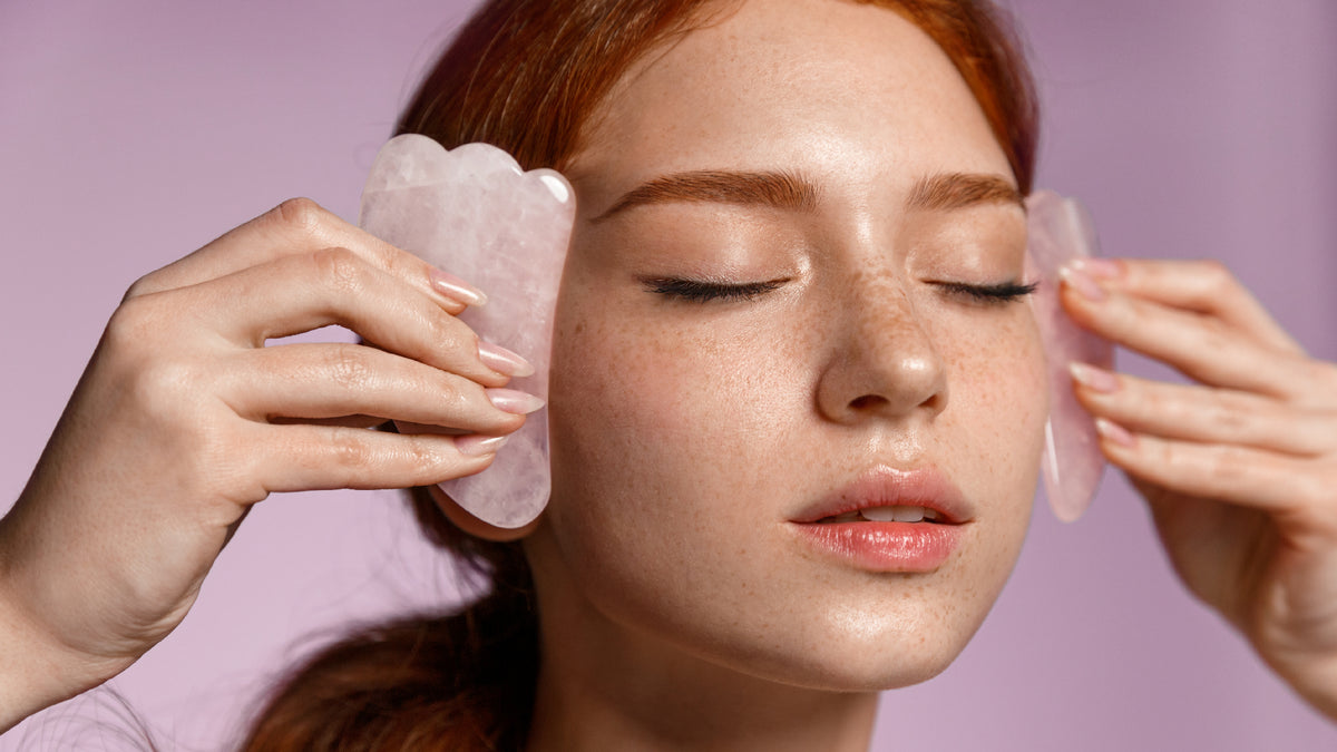 redhead woman on lilac background using gua sha to massage face
