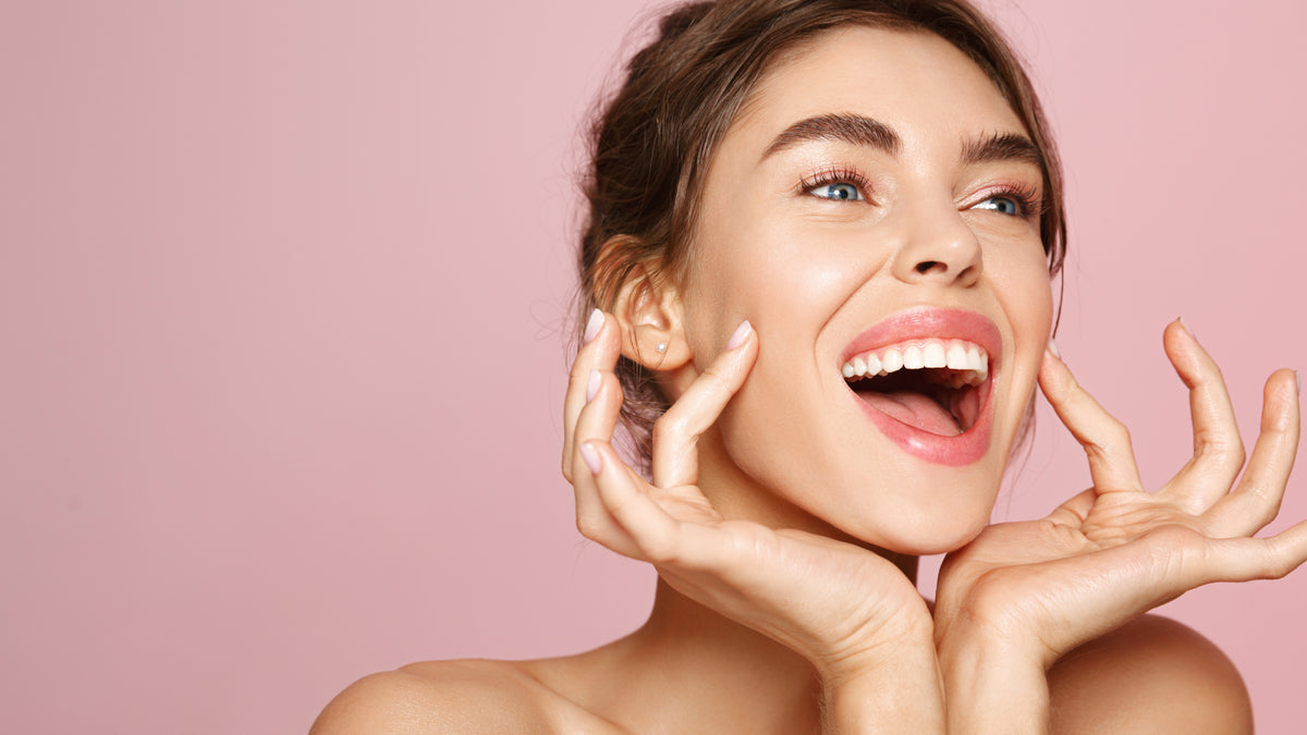 brunette girl on pink background laughing, fingers on face