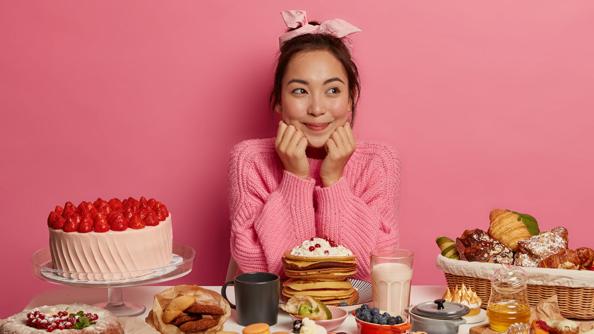 Happy girl on pink background with table full of treats and cakes