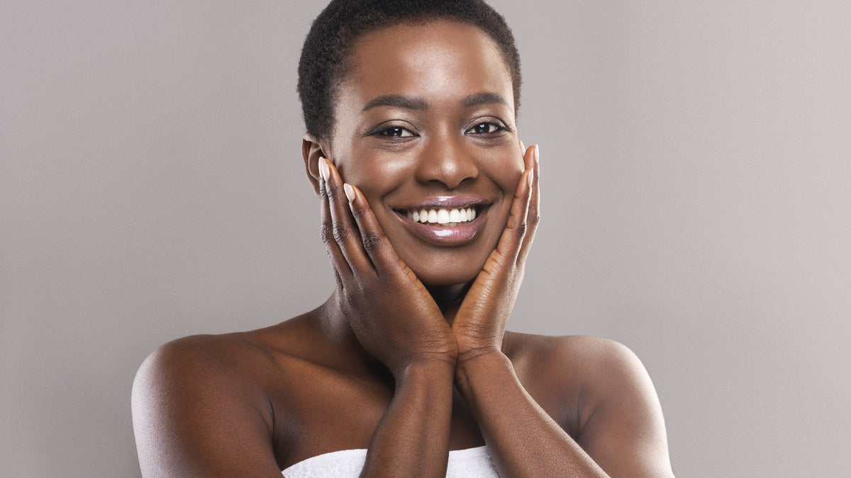 young black woman with dewy skin touching face and smiling