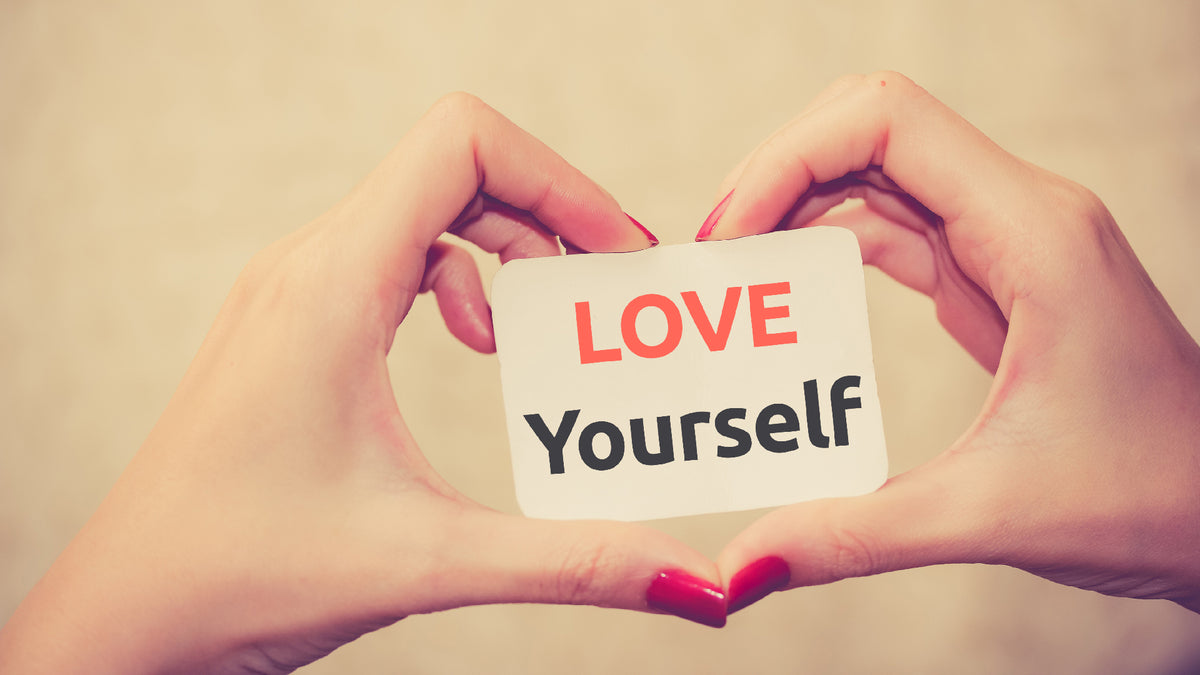 pair of hands making heart shape holding love yourself card