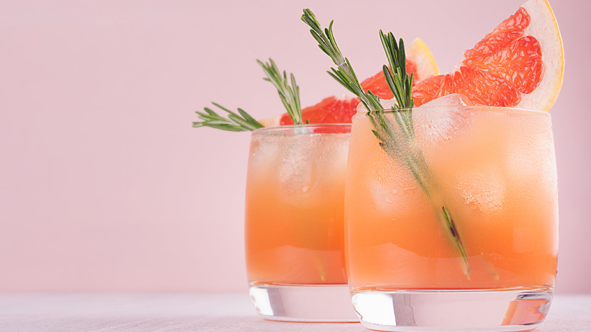 two grapefruit cocktails on pink background