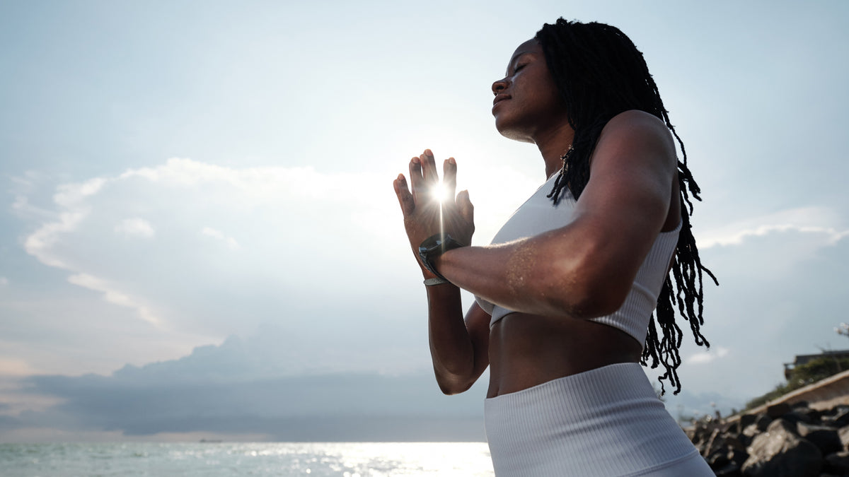 black woman relaxing, practising yoga by the ocean
