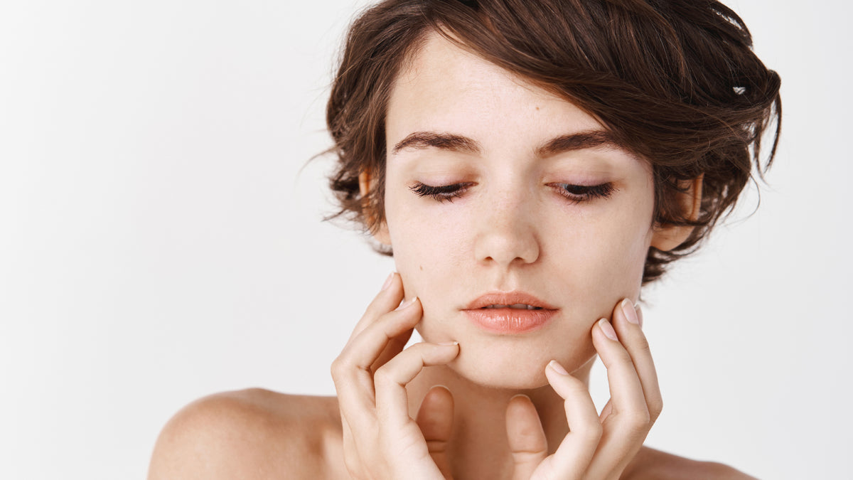 woman with short dark hair with great skin, touching face
