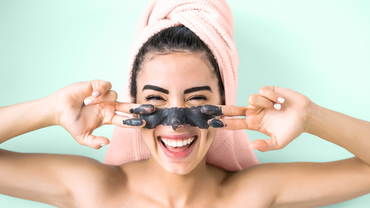brunette girl with towel on head and charcoal face wash on skin