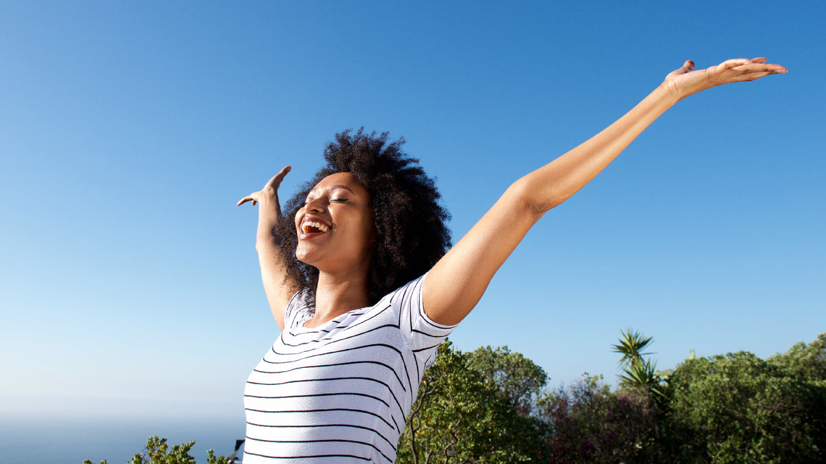 black women standing in sunshine with arms in the air