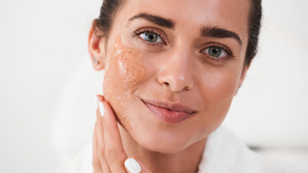 young brunette woman applying scrub to face