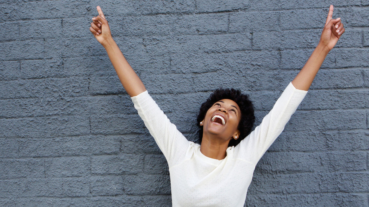 black girl in front of wall laughing with arms in the air