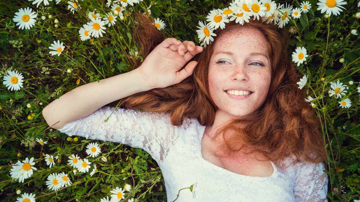 Redhead with beautiful skin lying in field of large daisies