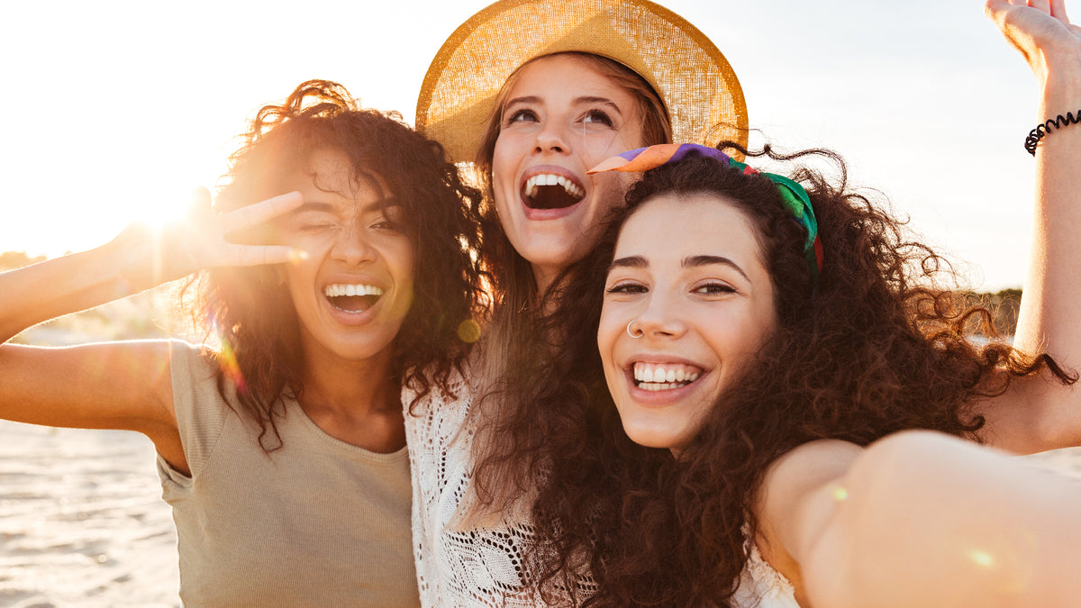 three girlfriends on a beach laughing and taking a selfie