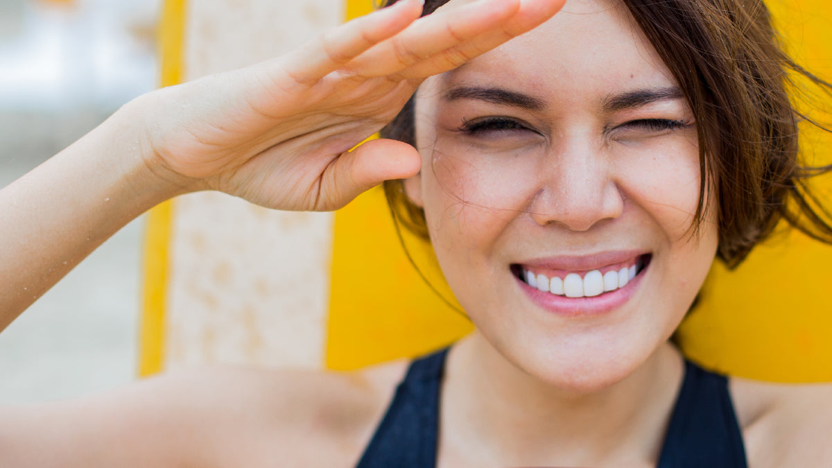 close-up brunette girl on beach squinting up into sun