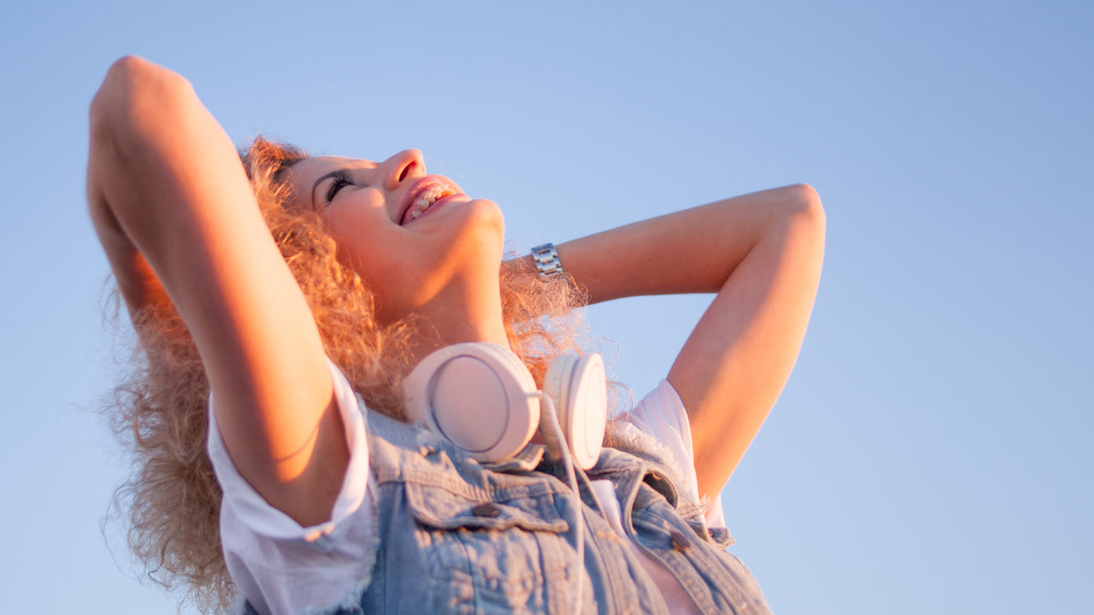 white girl with headphones standing outside on sunny day looking up at sky