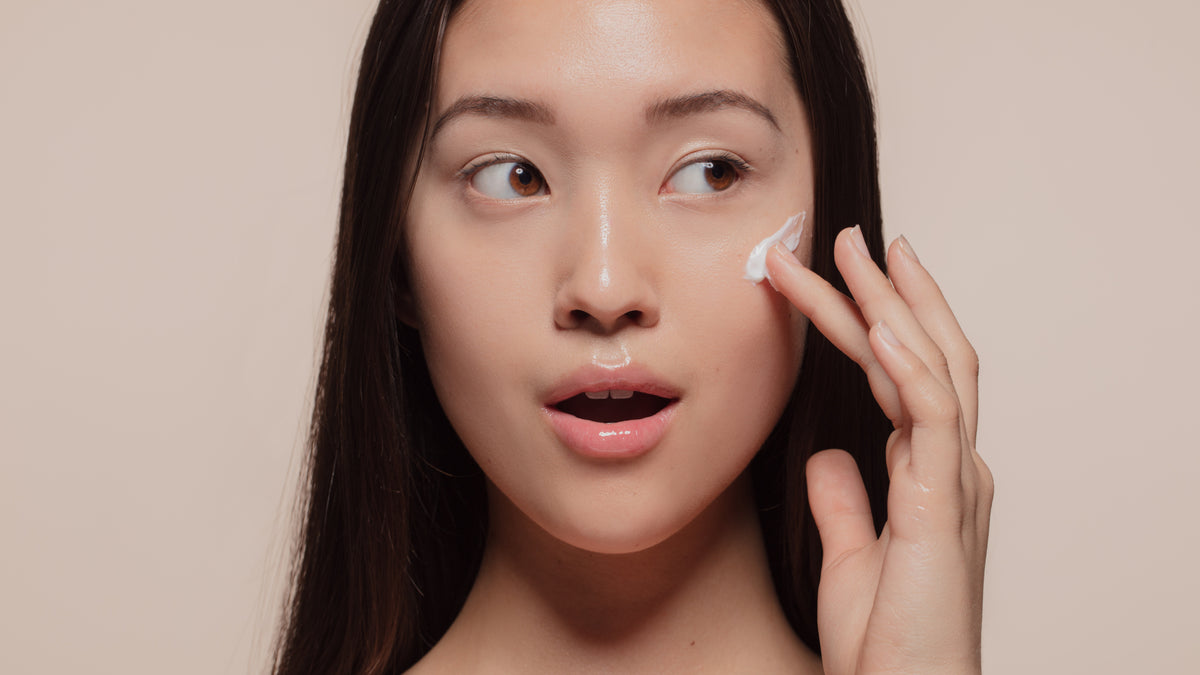 asian woman with great skin, applying face cream to cheek