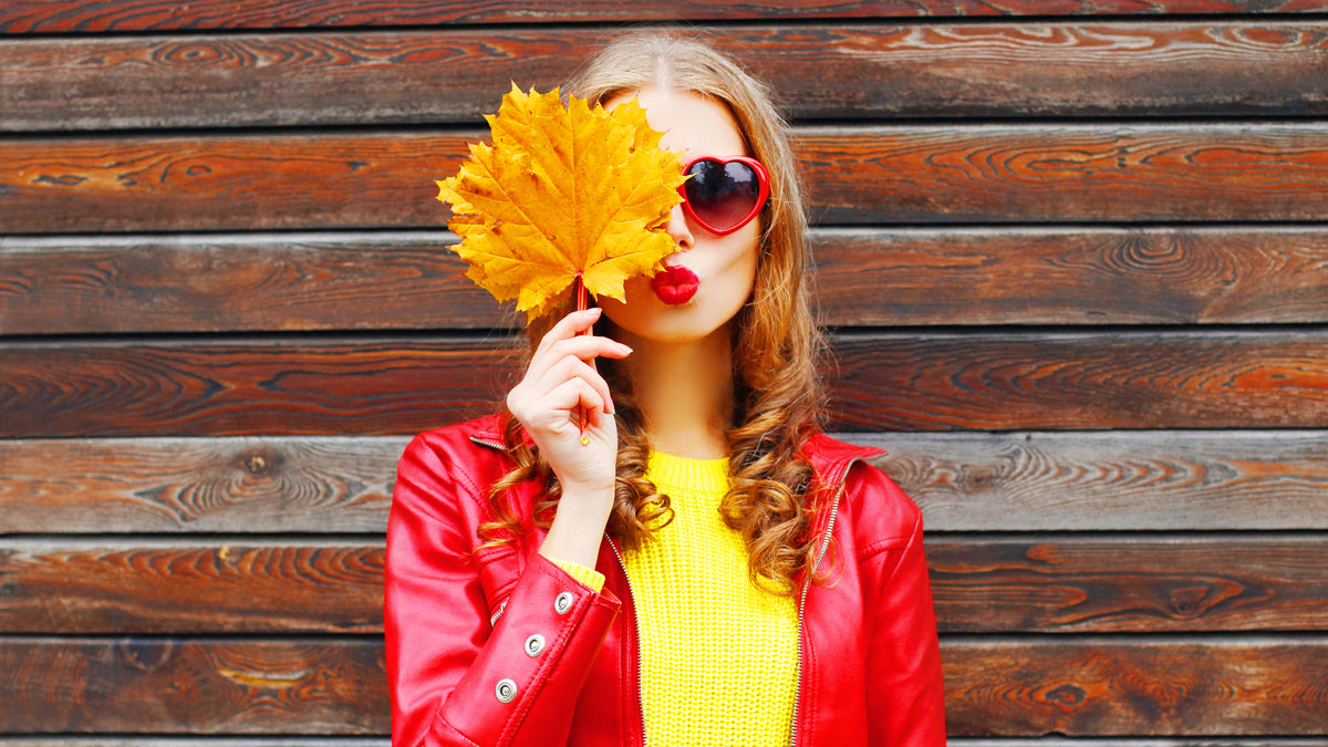 girl blowing kiss holding fall-colored leaf