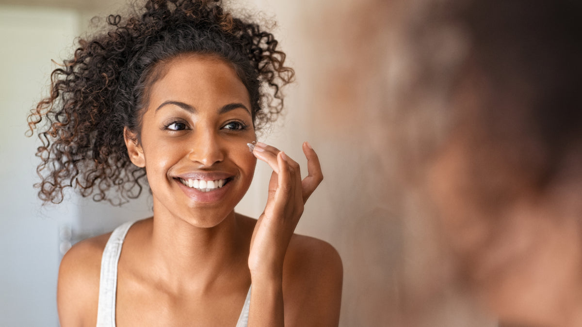 beautiful black girl applying face cream in mirror