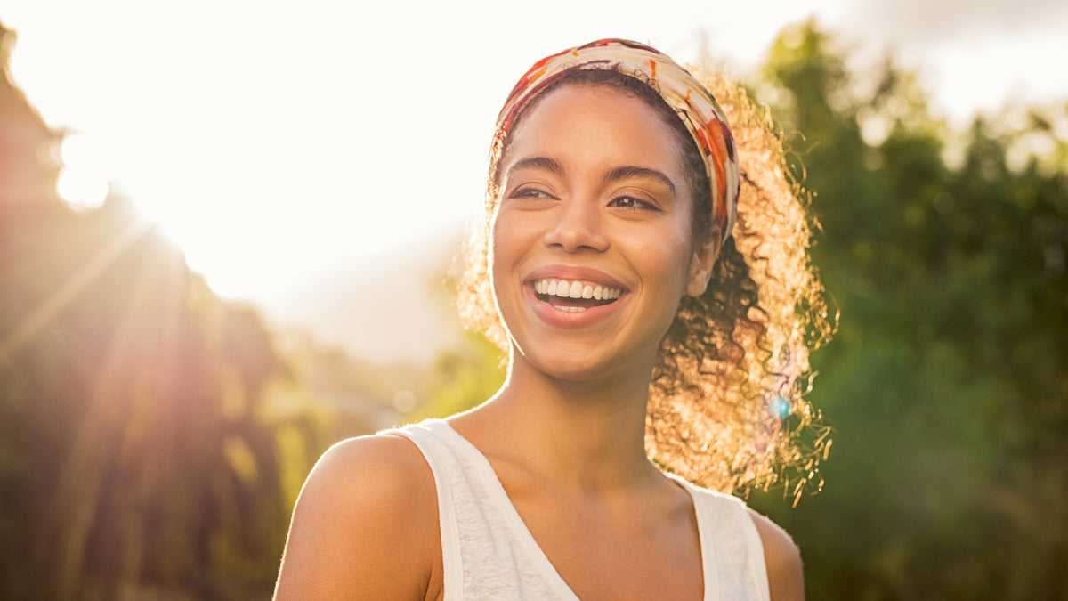 Black girl with great skin, smiling with sun behind her