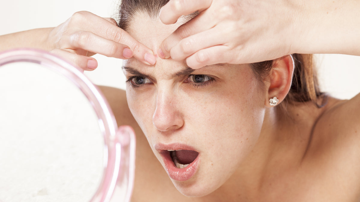 girl looking in the mirror and checking a pimple