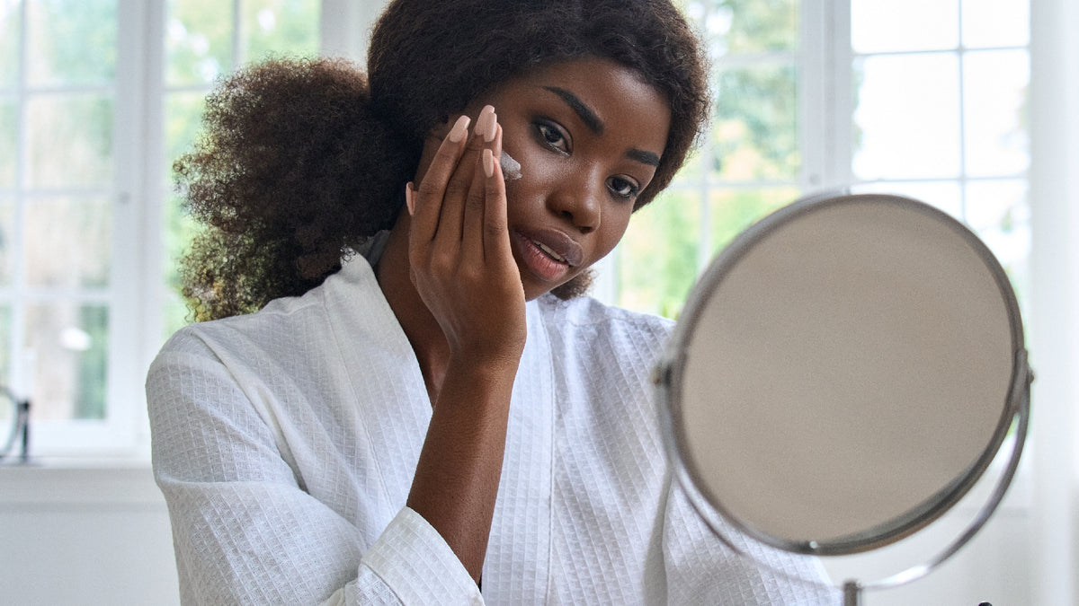 black girl in white robe looking at skin in mirror
