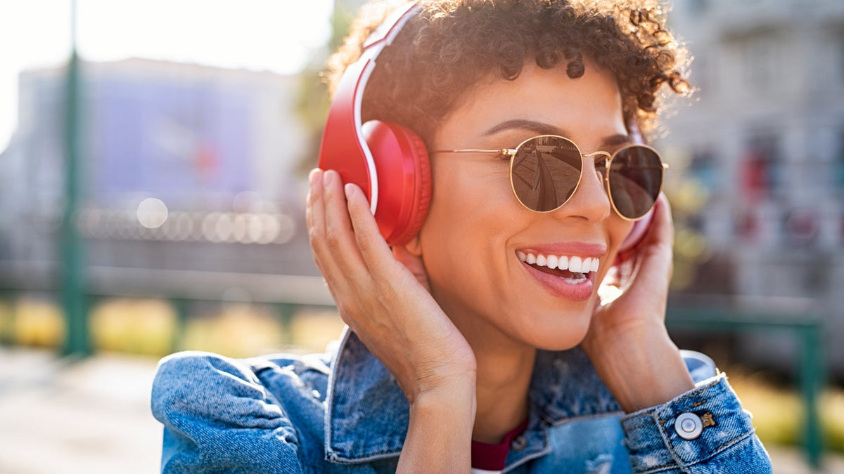 young black woman laughing in sunshine with sunglasses and headphones