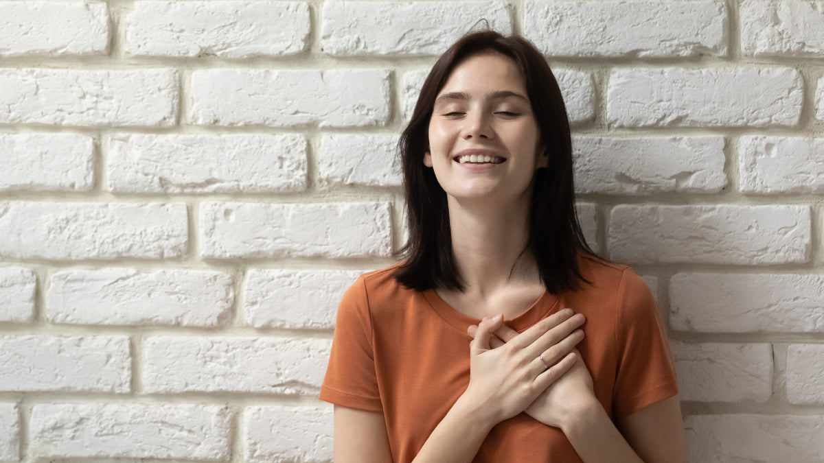 young brunette woman again wall making love sign with hands over heart