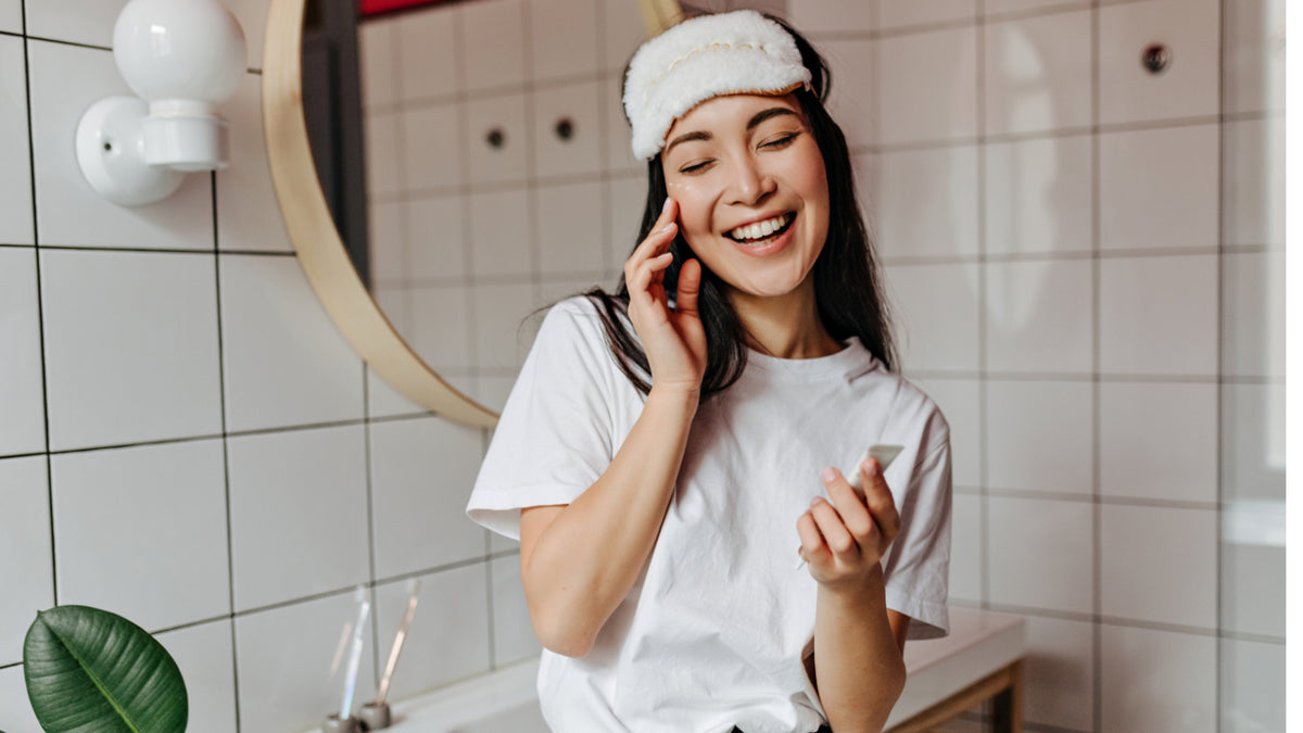 brunette girl in bathroom with sleep mask applying face product