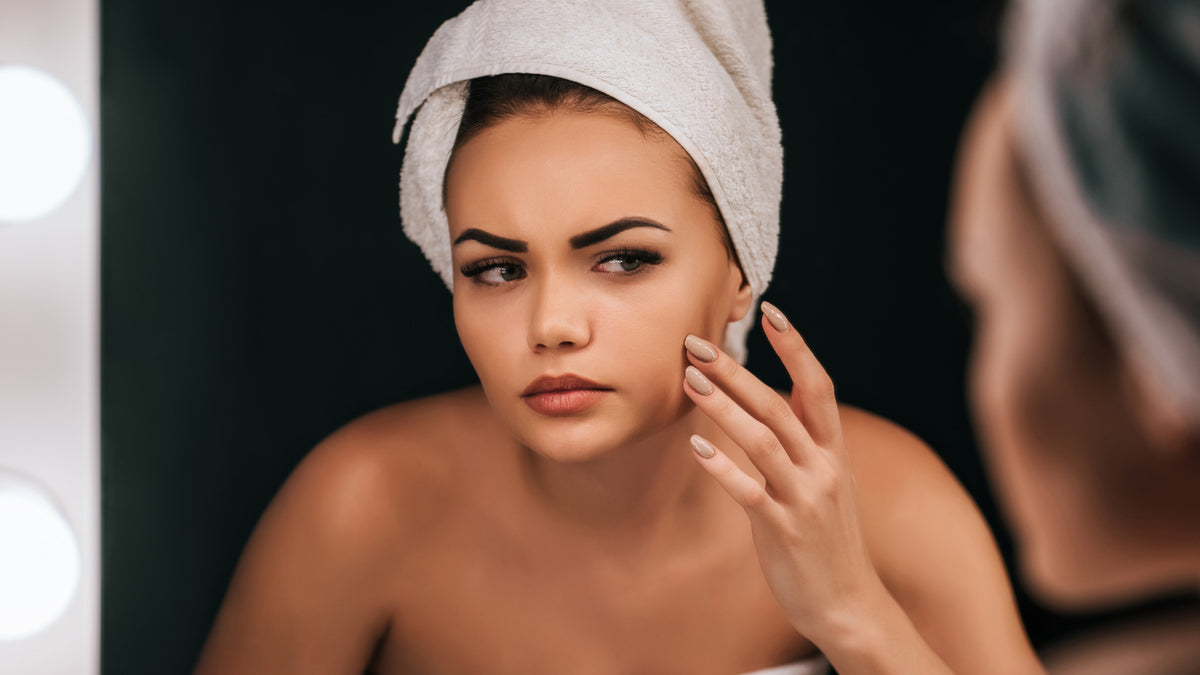 beautiful white girl with towel on head examining skin in mirror