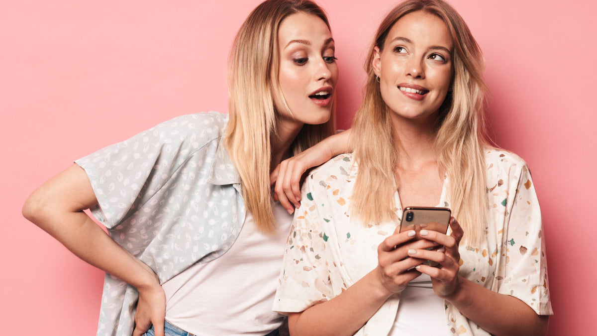 two blonde friends looking at phone and thinking, smiling