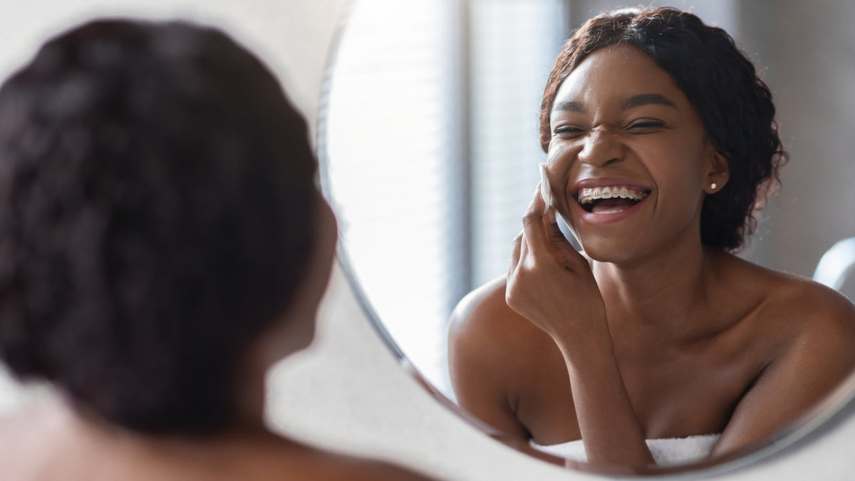 young black woman applying face products in the mirror
