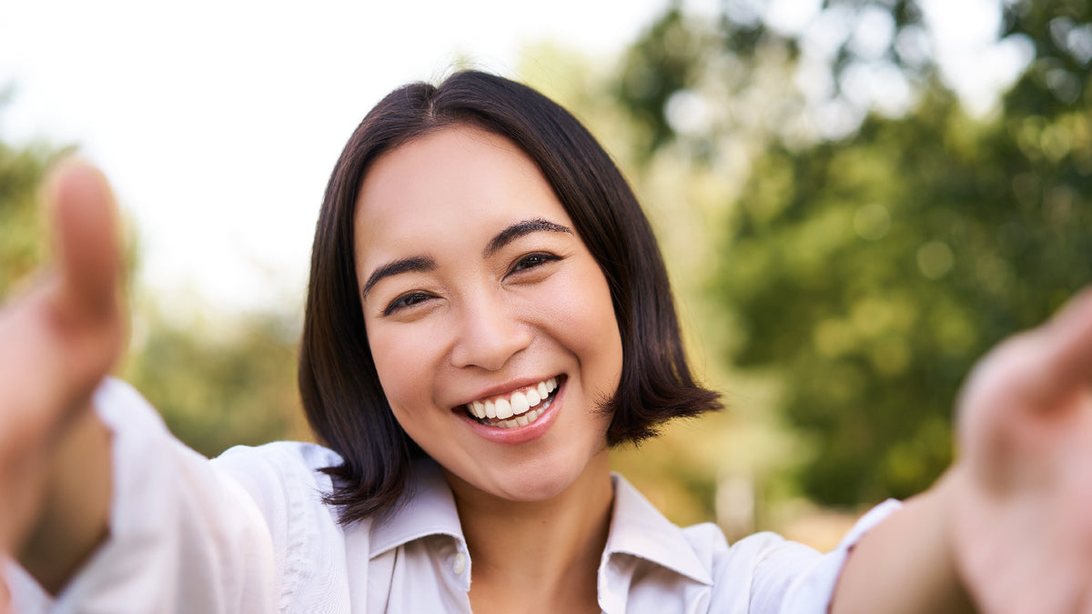 brunette girl smiling while taking a selfie outside