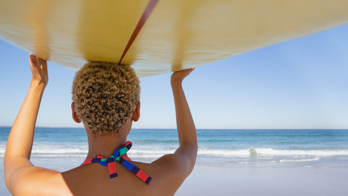 back of woman's head holding surf board on beach