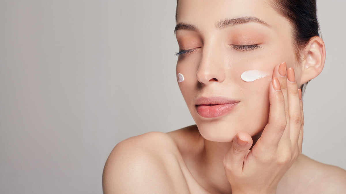 brunette girl on gray background applying moisturizer to skin