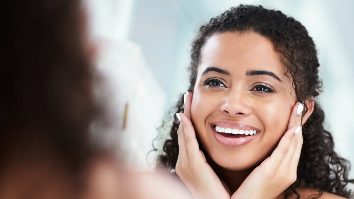 young woman touching skin and smiling in mirror