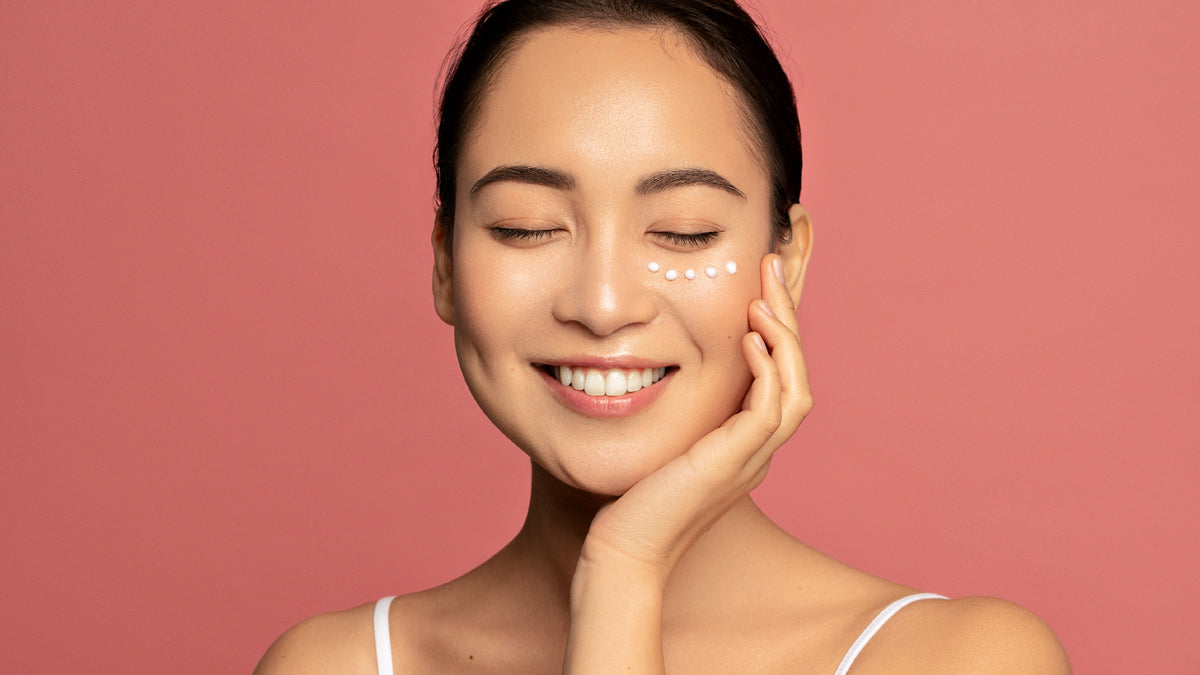 Brunette girl smiling with great skin and dots of eye cream under one eye