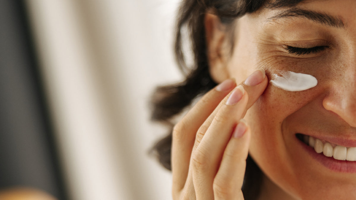 close-up of brunette woman applying face cream to cheek
