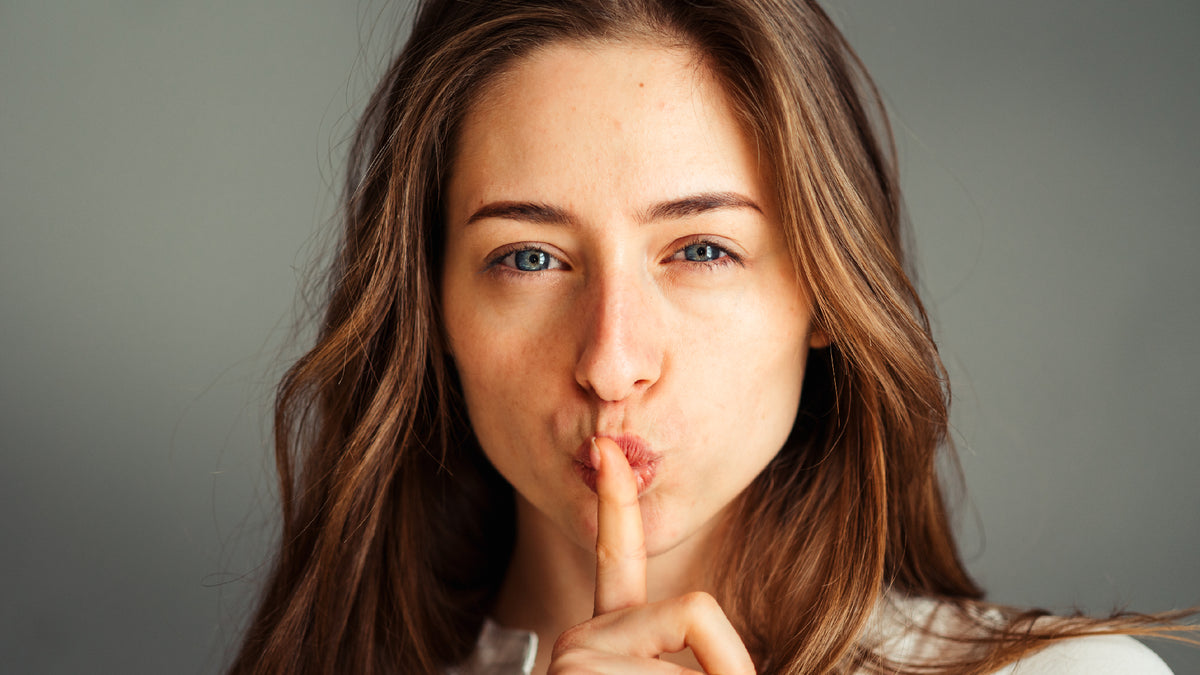 young brunettte woman wearing makeup making shush sign