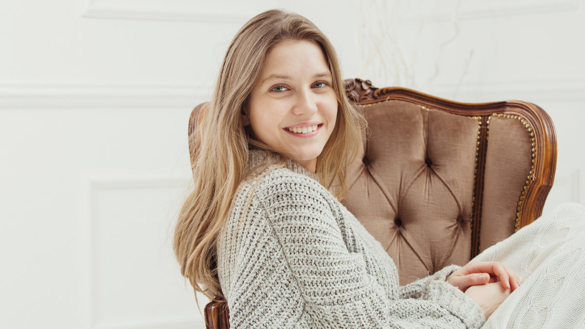 young blonde woman with natural makeup sitting on chair and smiling at camera