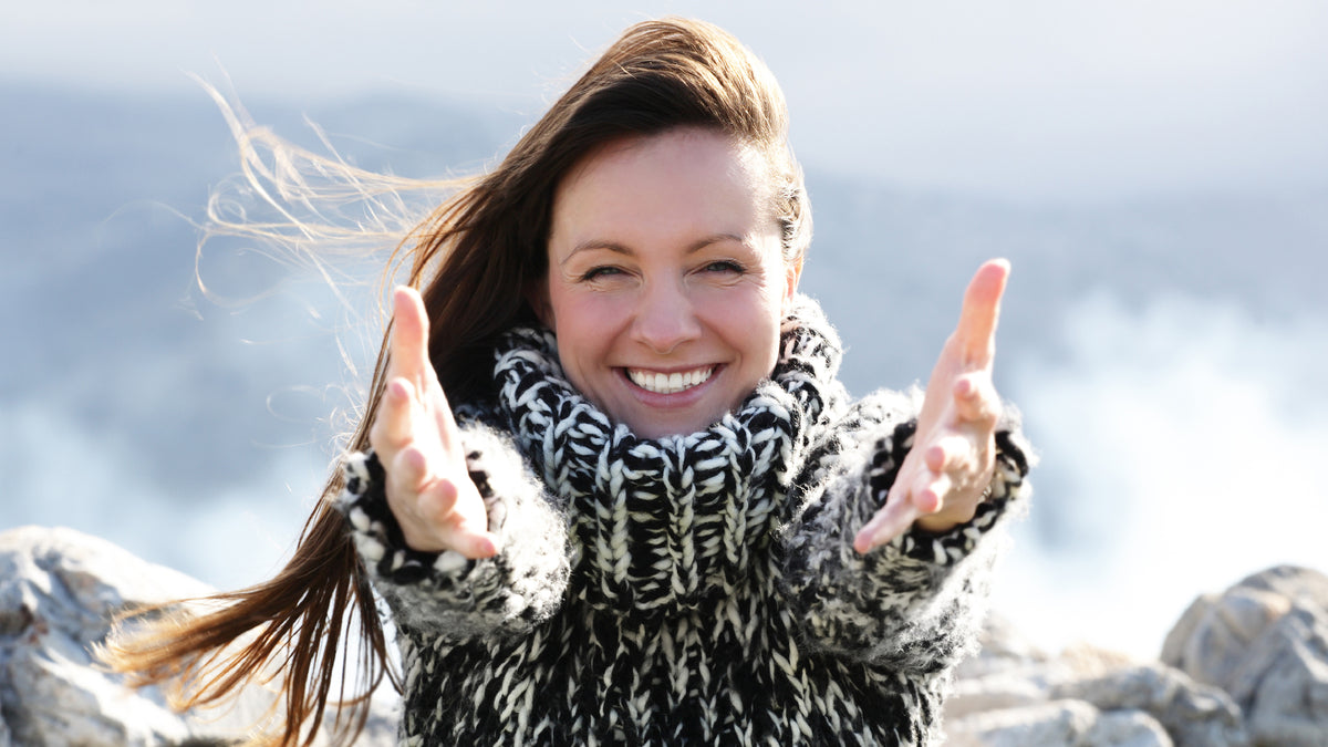 brunette woman smiling outside with hands to camera
