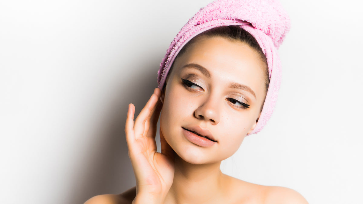 Woman touching her face with beautiful skin and pink towel on her head